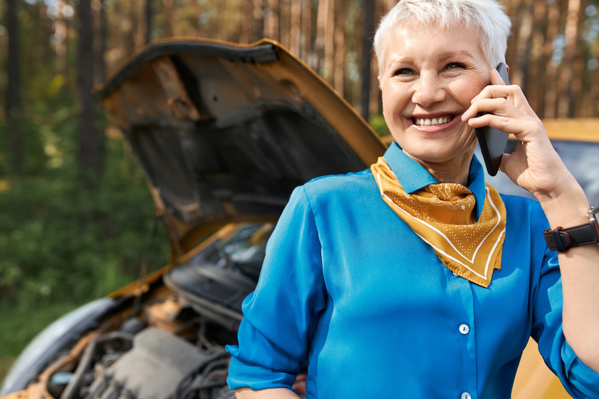 Pessoa ao telefone próximo a um carro com o capô aberto, representando assistência 24 horas